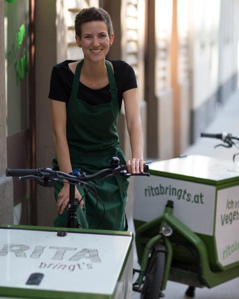 Rita Huber sitzt auf einem Rita bringts Lastenrad und lächelt in die Kamera