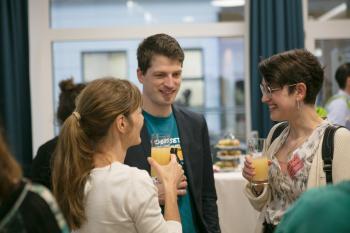 Drei Personen reden miteinander und halten jeweils ein Glas Orangensaft in der Hand