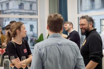 Zwei Männer, eine Frau, stehen um eine Tisch und unterhalten sich. 