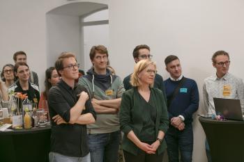 Einige Personen aus dem Publikum, darunter BM Leonore Gewessler, die alle interessiert auf die Bühne schauen.