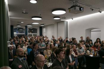 Der Eventspace ist voll mit Menschen, die interessiert richtung Bühne blicken