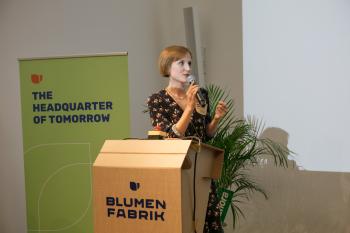 Mira Nograsek steht auf der Bühne hinter dem Pult und spricht in ein Mikrophone