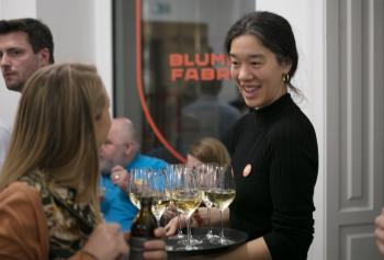 Eine Kellnerin lächelt und trägt Gläser mit Weißwein auf einem Tablett.