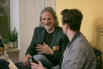 Zwei Männer sitzen am Sofa und unterhalten sich.