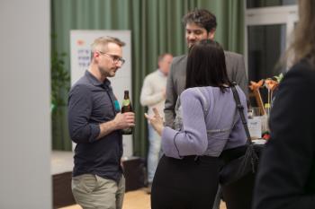 Drei Personen stehen neben der Bühne und unterhalten sich. Sie haben Getränke in der Hand.