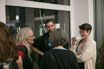 Vier Personen stehen im Kreis und reden miteinander. Eine Frau hat eine Tasse in der Hand woraus sie trinkt.