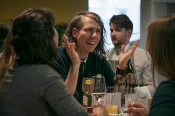 Im Fokus ist ein Mann mit längeren Haaren, der seine Hände in die Höhe hält und lacht.