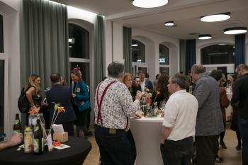 Im Eventspace stehen Besucher:innen um Stehtische und reden miteinander