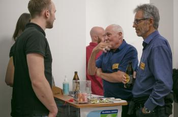 Beim Infostand von GLOBAL 2000 tauschen sich zwei Männer mit den Mitarbeiter:innen aus.