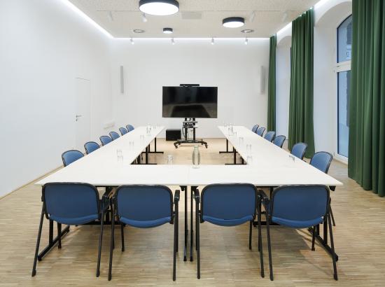 Meetingraum mit Tisch, Stühlen und Bildschirm