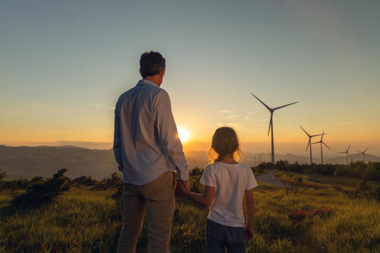 Mann und Kind schauen in Landschaft mit Windräder, die Sonne geht auf oder unter
