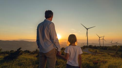 Mann und Kind schauen in Landschaft mit Windräder, die Sonne geht auf oder unter